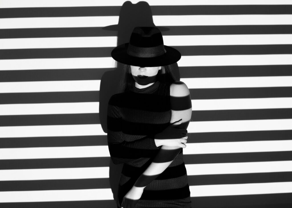 Elegant black and white portrait of a woman in a hat with projected stripes creating a dramatic effect.